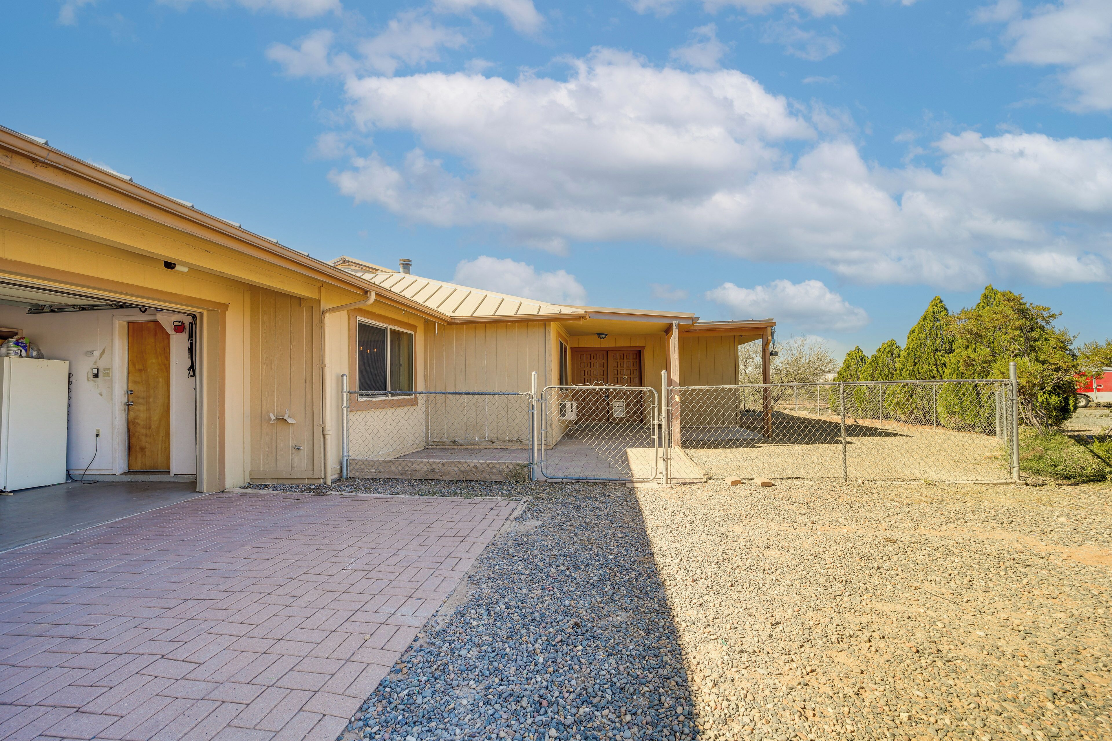 A building with a covered entrance, a gravel driveway, and a fenced area.