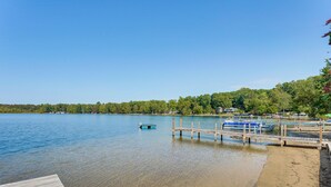 Eine hölzerne Anlegestelle, die sich in ruhiges Wasser erstreckt, umgeben von blauem Himmel und einer bewaldeten Uferlinie.