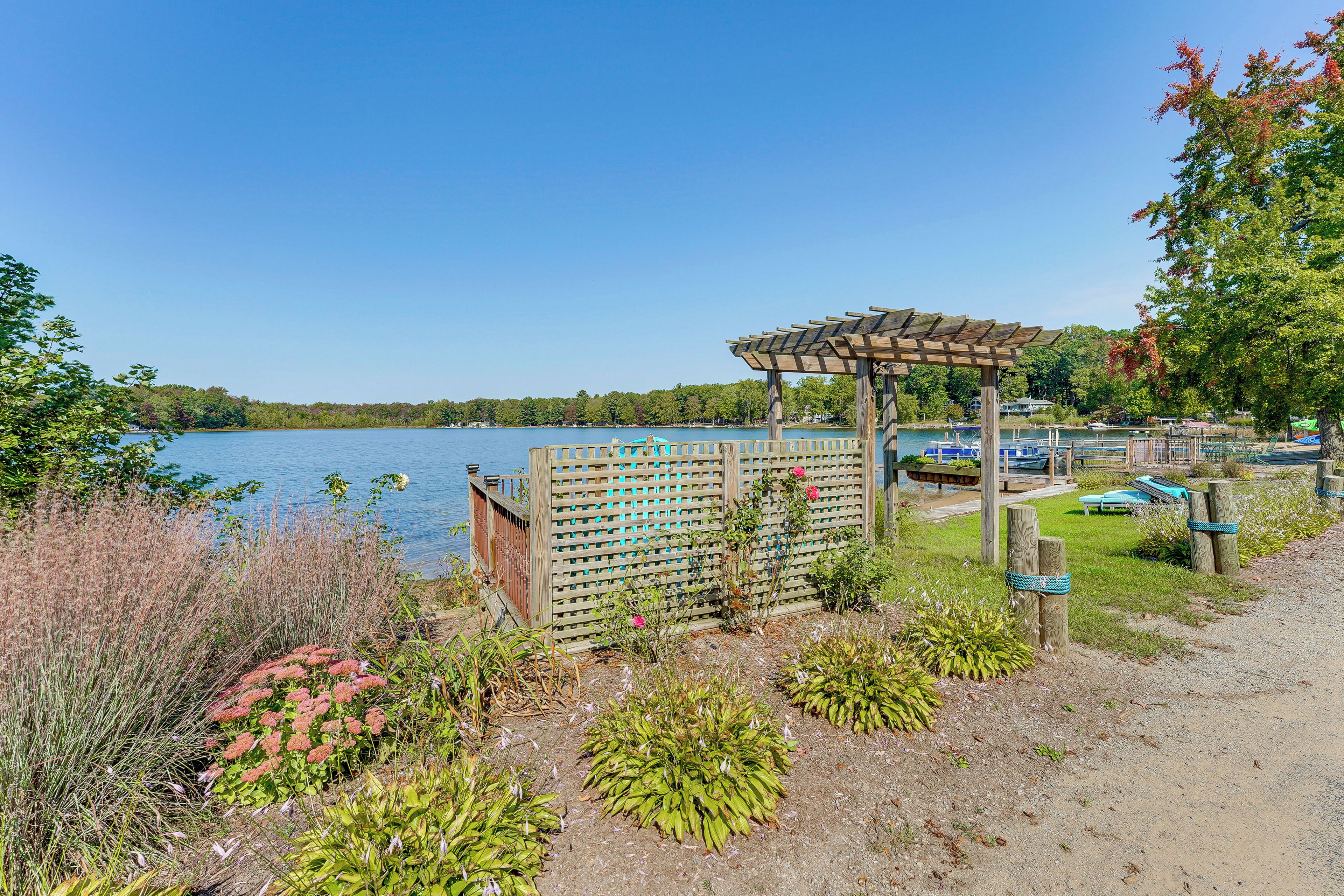 Un jardin au bord du lac, agrémenté d’une pergola, d’une clôture en bois et d’un quai avec des bateaux.