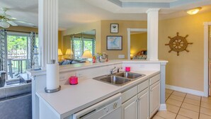 A modern kitchen with white cabinetry, a double sink, and a large window. - Golfer's Haven: Calabash Condo, 9 Mi to Beach (Calabash)