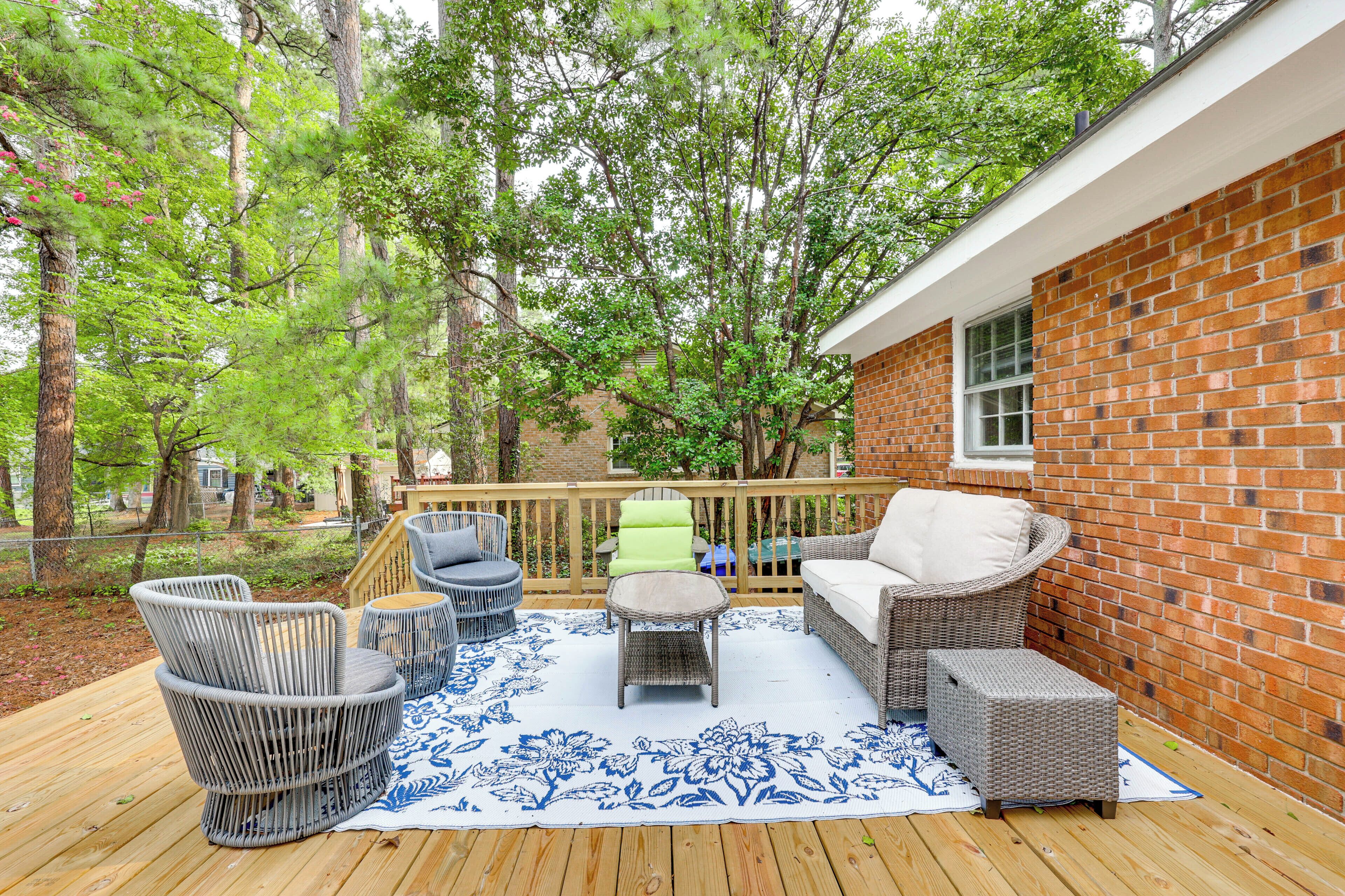 A covered outdoor deck with wicker furniture, a blue patterned rug, and a brick wall.