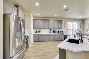 A modern kitchen with grey cabinets, a stainless steel refrigerator, and a central island with a sink.