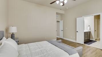 A bedroom with a bed, a nightstand, a lamp, a ceiling fan, and an open door leading to a bathroom.