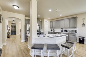 A modern kitchen with a central island, bar stools, and a view into the dining area.