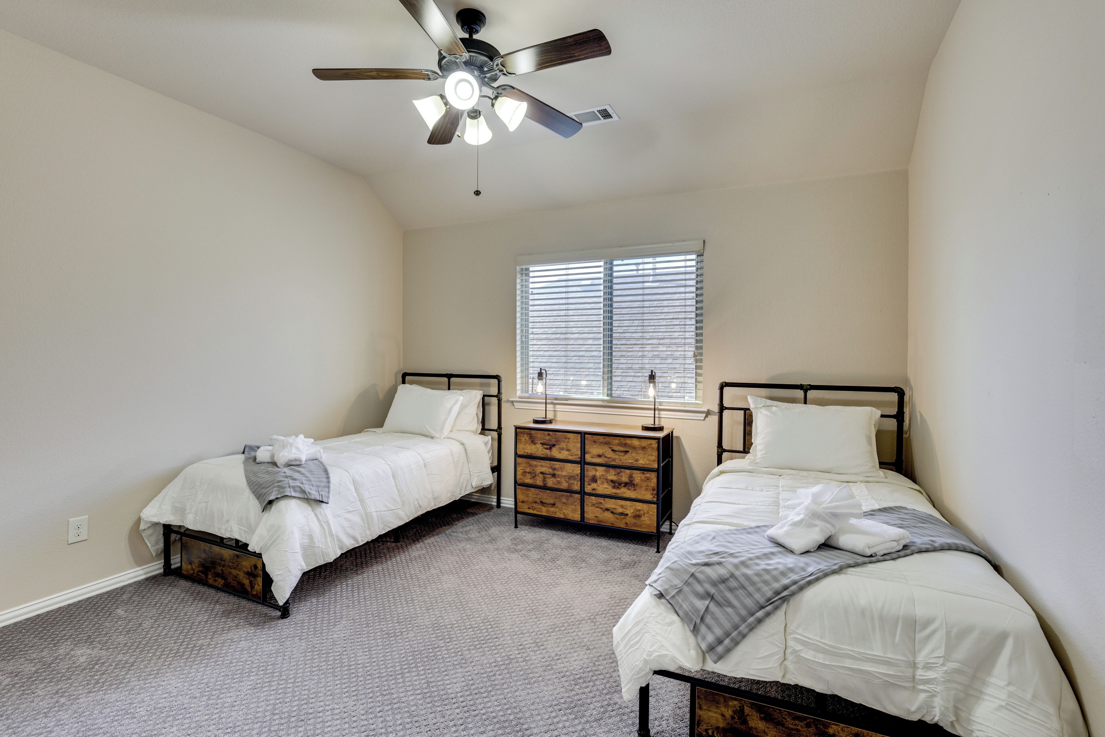 A bedroom with two beds, a ceiling fan, a dresser, and a window with blinds.