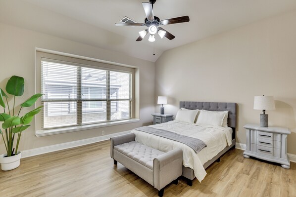 Ein Schlafzimmer mit einem Bett, Nachttischen, einer Bank, einem Deckenventilator und einem Fenster mit Jalousien.