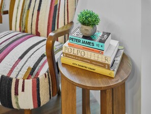 A stack of books on a small wooden table with a potted plant on top, placed next to a striped chair. - 4 bedroom accommodation in Windermere (Windermere)