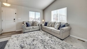 A living room with a grey sectional sofa, a patterned rug, and a city view through the windows. - 'mountain Family Getaway' in Colorado Springs! (Colorado Springs)