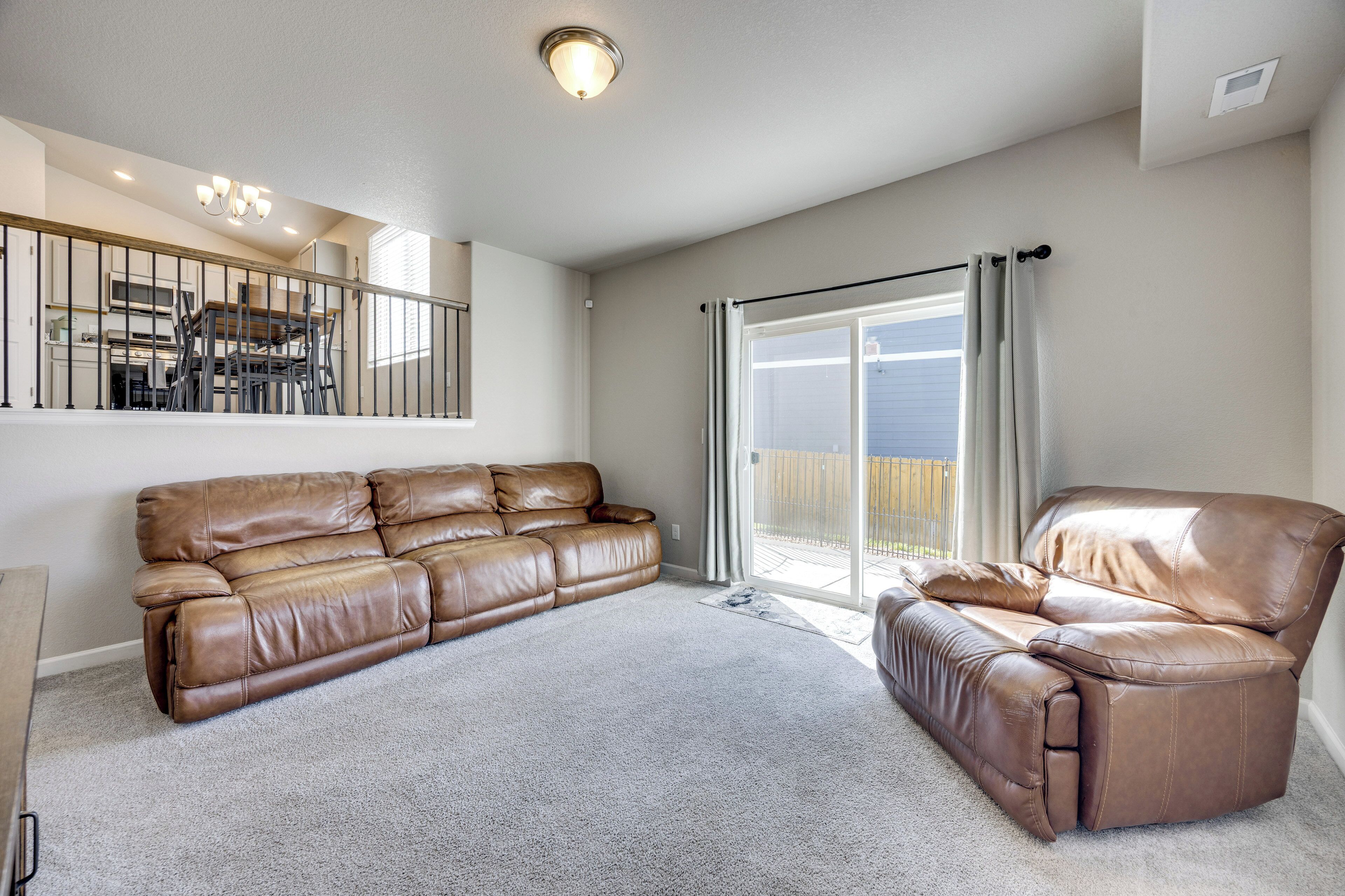 A spacious living room with a large brown leather sofa, a smaller leather armchair, and a dining area with a wooden table and chairs.