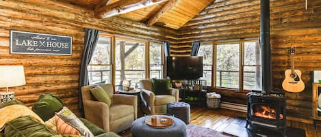 A log cabin interior with a fireplace, comfortable seating, and a television.