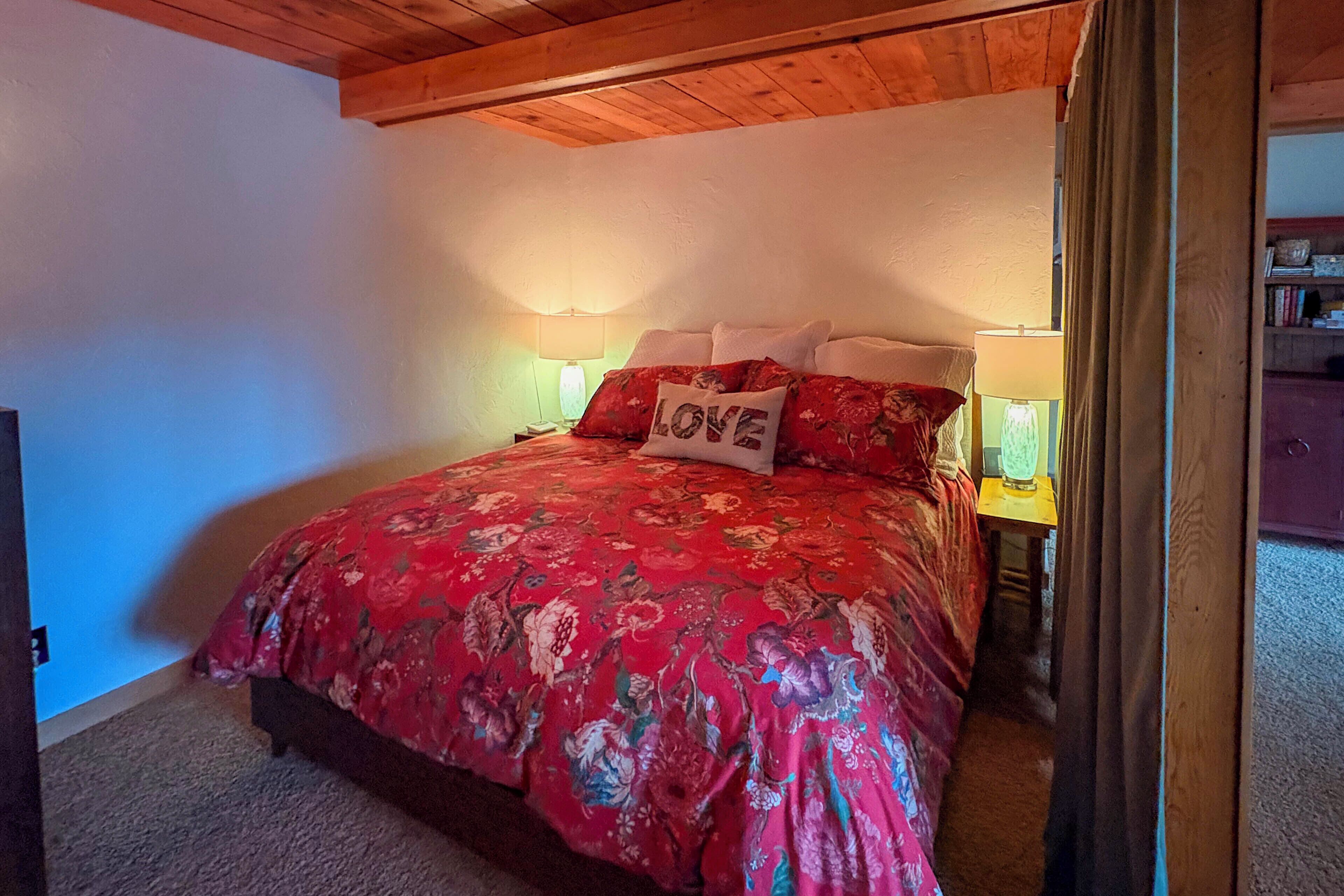 A bedroom with a floral bedspread, two bedside lamps, a nightstand, and a pillow with the word "LOVE".