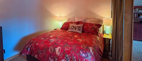 A bedroom with a floral bedspread, two bedside lamps, a nightstand, and a pillow with the word "LOVE".