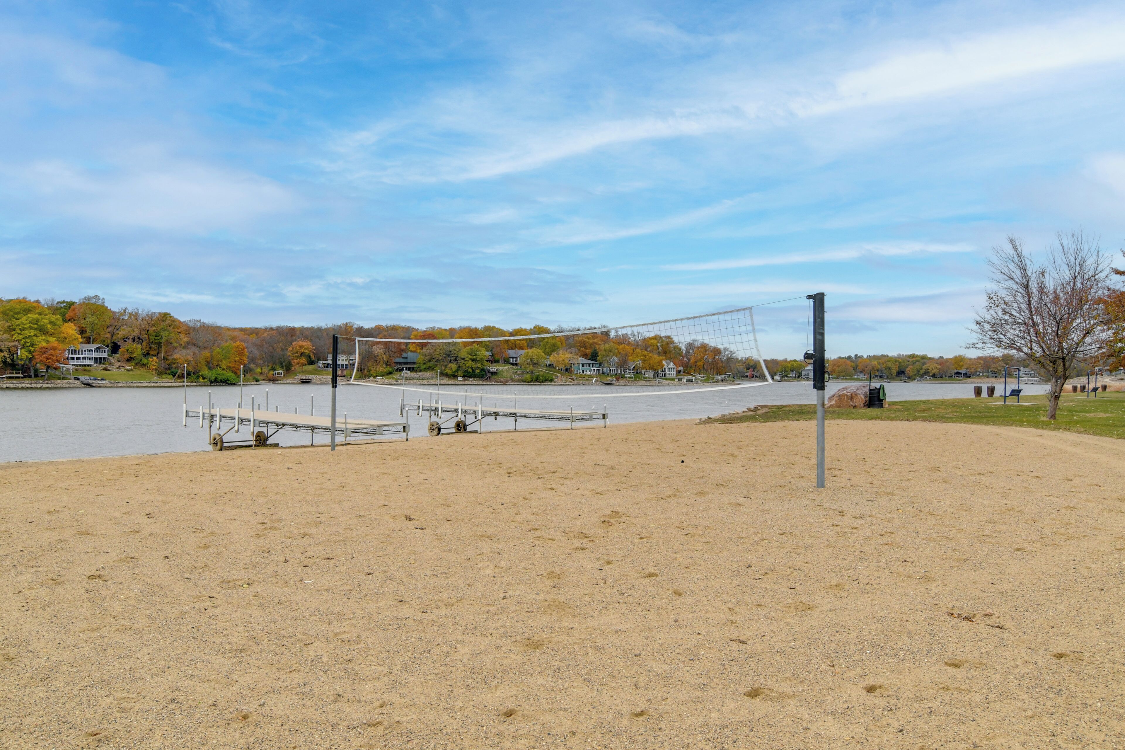 Une plage de sable avec un filet de volley-ball, une jetée et une étendue d’eau en arrière-plan.