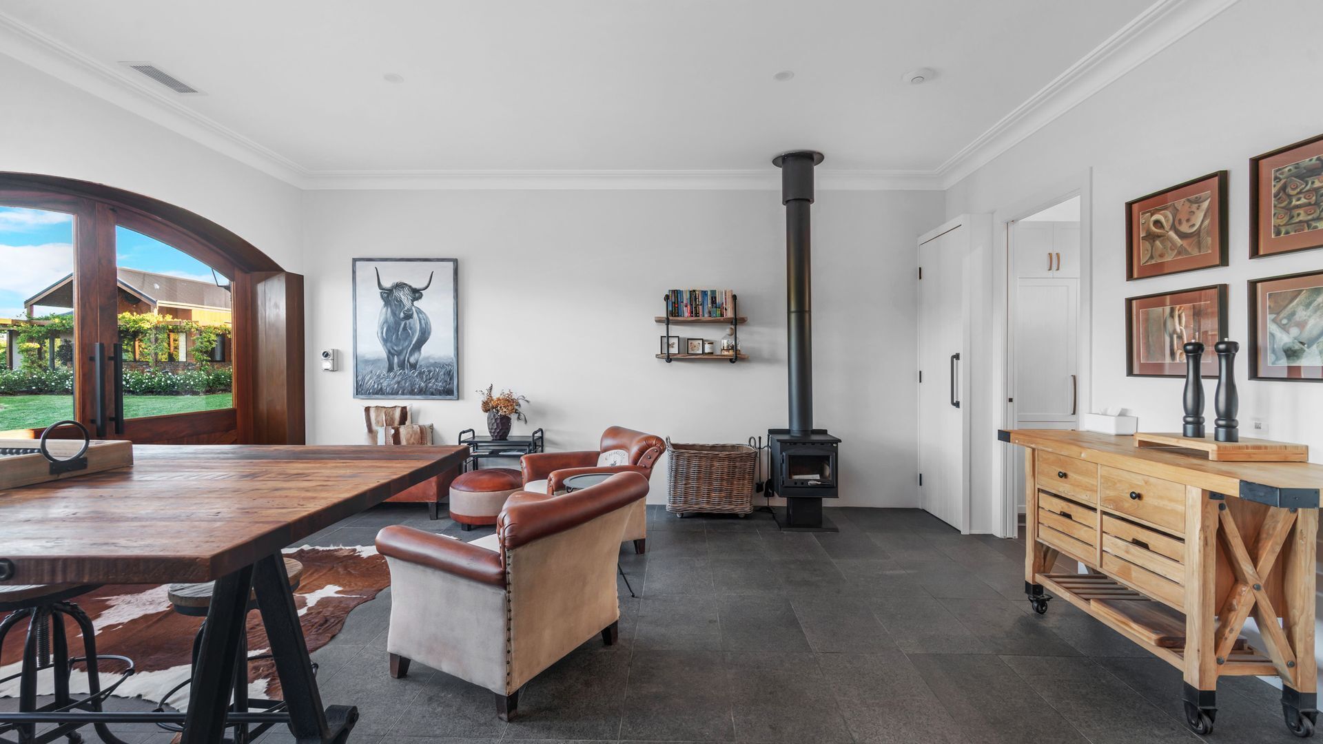 Ein großzügiger Wohnbereich mit einem großen Holzesstisch, Ledersofas, einem Kamin und Blick ins Freie.