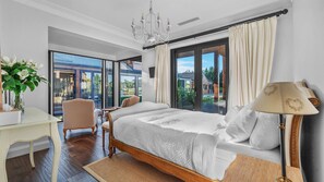 Une chambre spacieuse dotée d’un grand lit, d’un bureau et d’une chaise, et offrant une vue sur un jardin et un bâtiment grâce à de grandes fenêtres.
