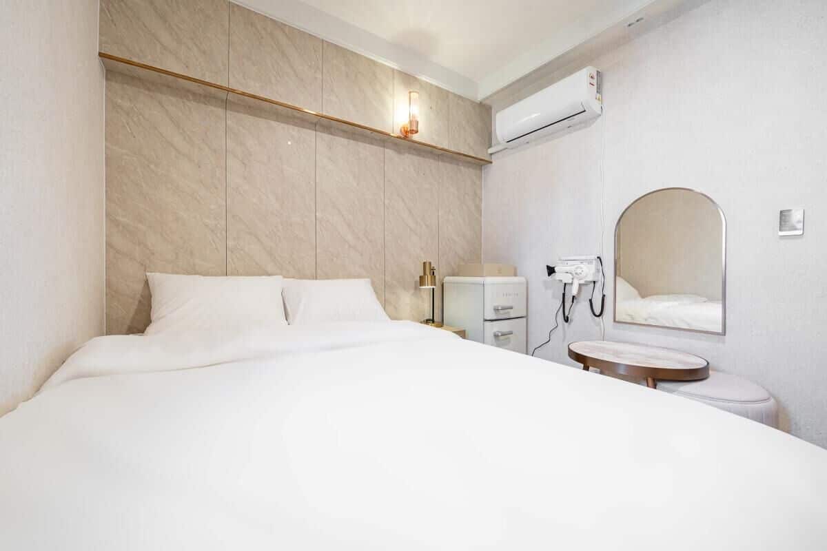 Habitación de hotel con una cama grande, una mesita de noche, un espejo, un inodoro y un aire acondicionado instalado en la pared.