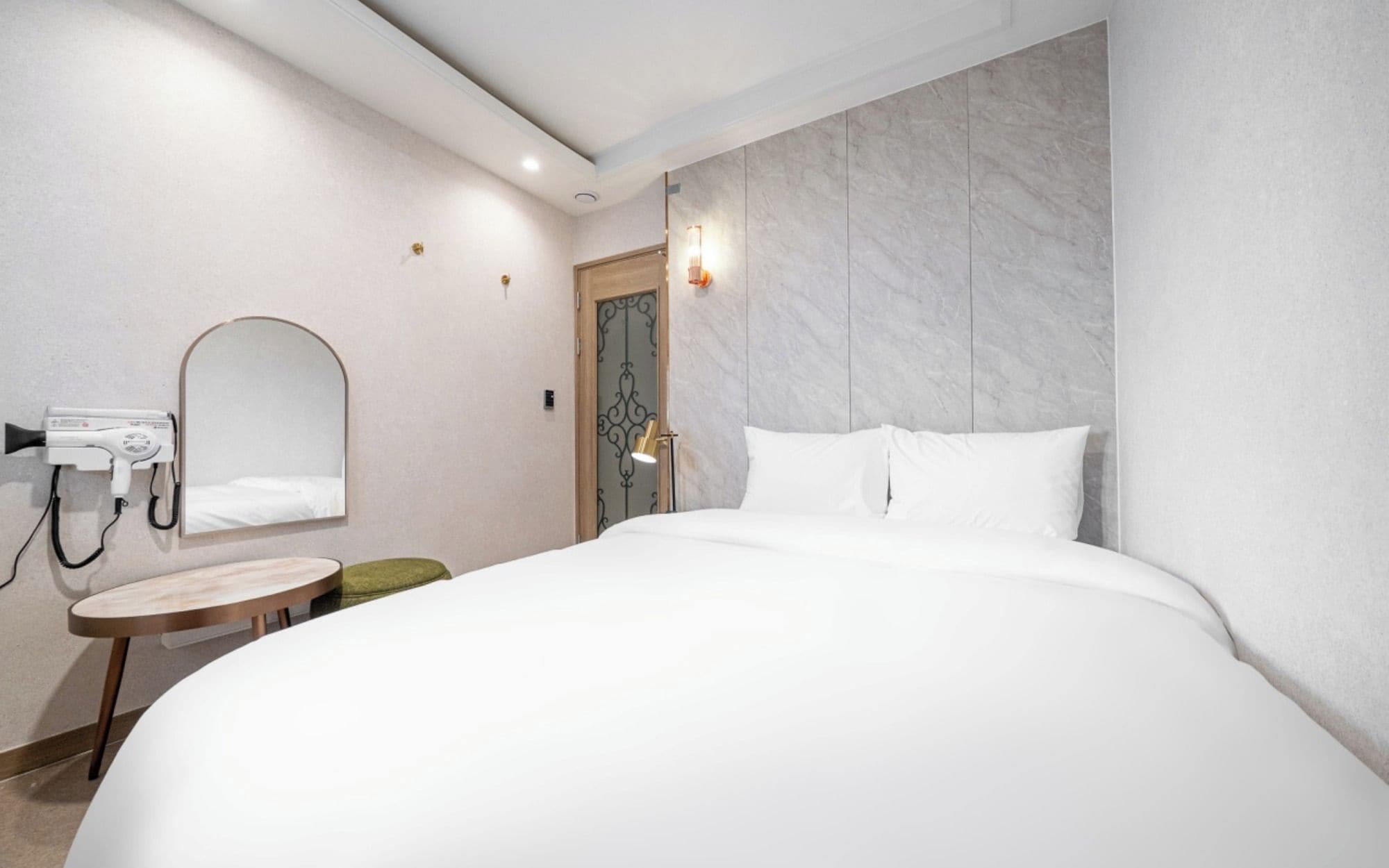 Hotellihuone, jossa on suuri sänky, pyöreä puinen pöytä, hiustenkuivaaja ja peili seinällä.