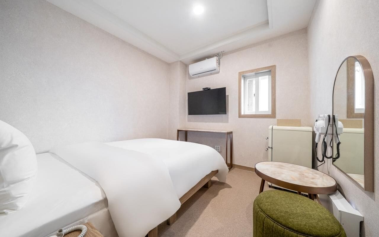 A hotel room with a bed, a small table, a mirror, a TV, and a hairdryer.
