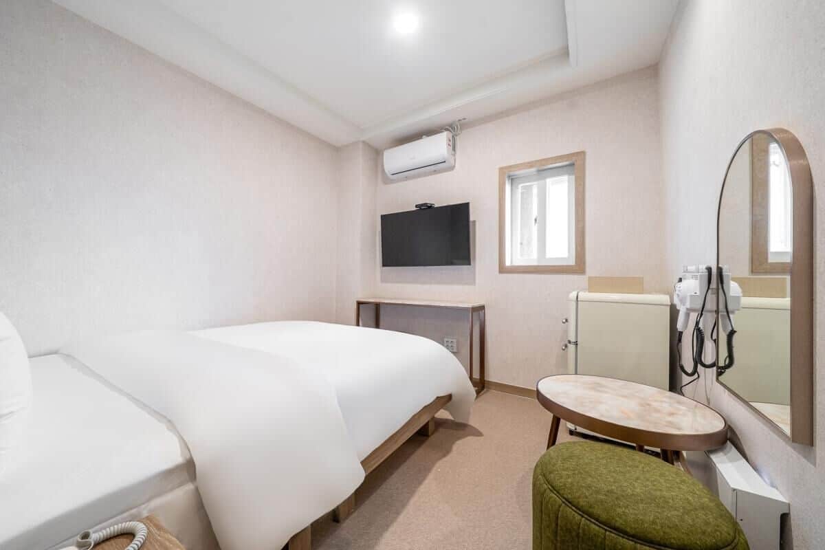 Ein Hotelzimmer mit Bett, einem kleinen Tisch, einem Spiegel, einem Fernseher und einem Fön.