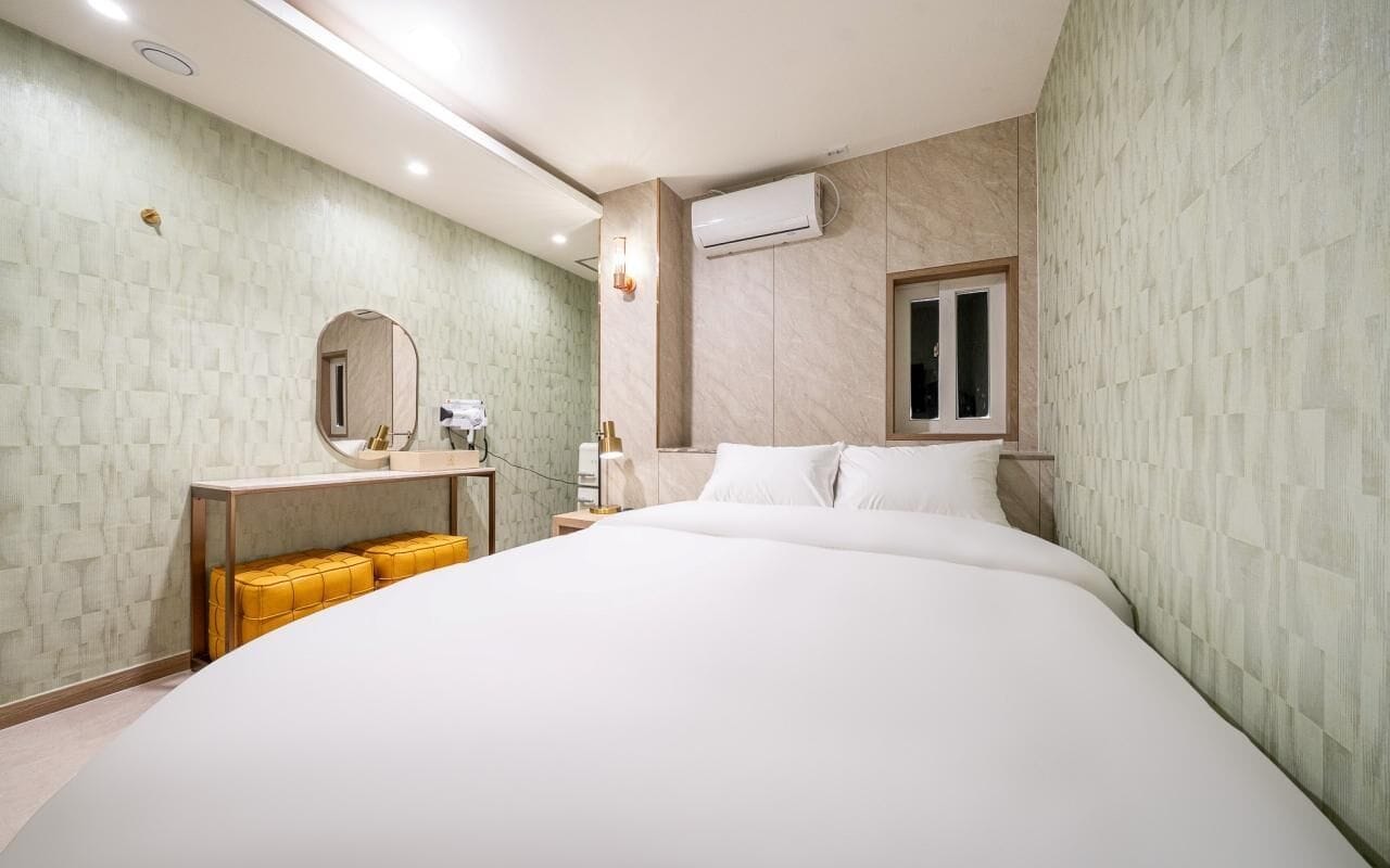 A modern hotel room with a large bed, a bedside table, a mirror, and an air conditioning unit.