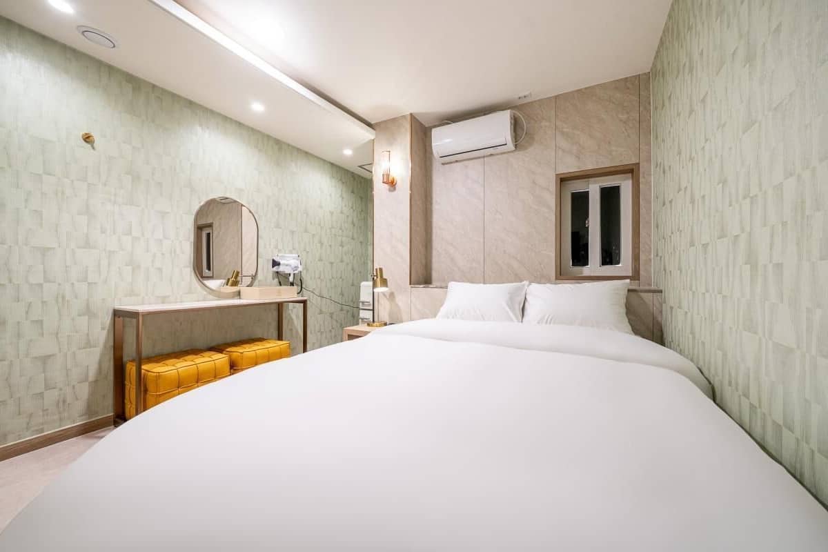 Ein modernes Hotelzimmer mit einem großen Bett, einem Nachttisch, einem Spiegel und einer Klimaanlage.