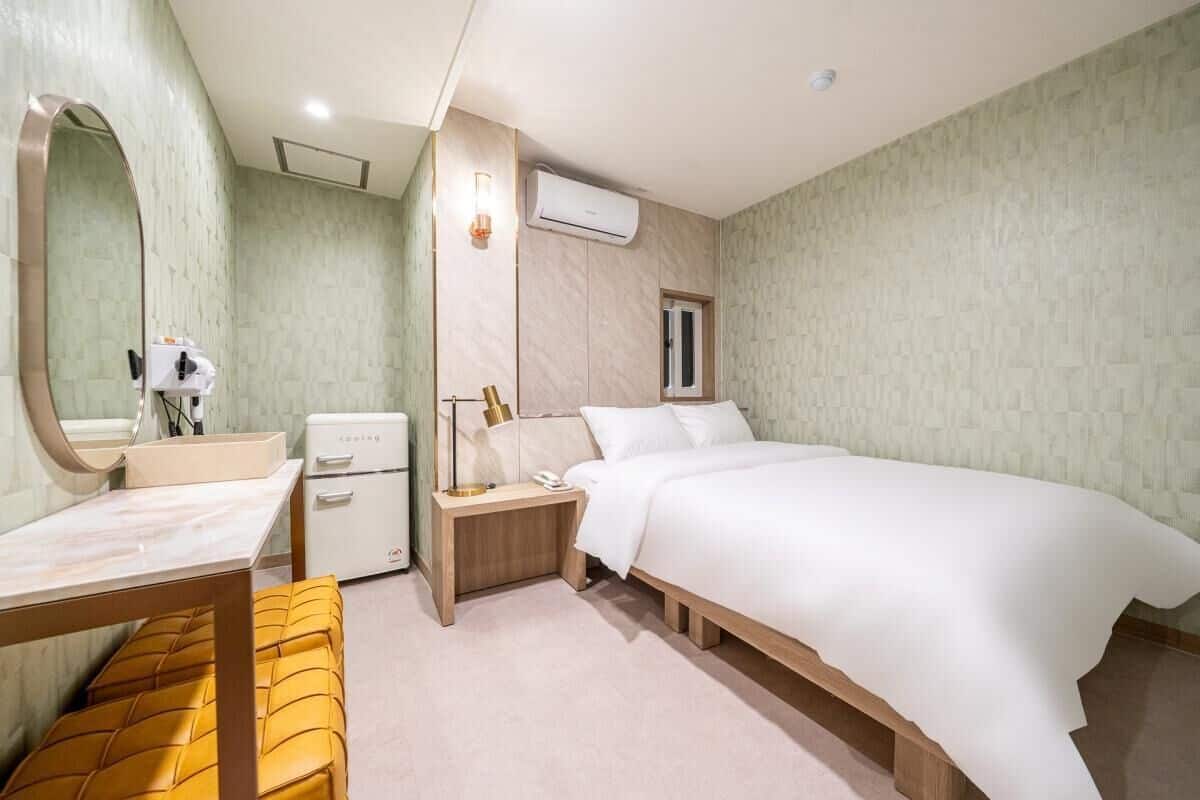 Una habitación de hotel con cama, mesita de noche, lámpara y espejo.