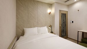 A hotel room with a bed, a nightstand, a lamp, a door with a decorative glass panel, and a small table. - The Stay (Seoul)