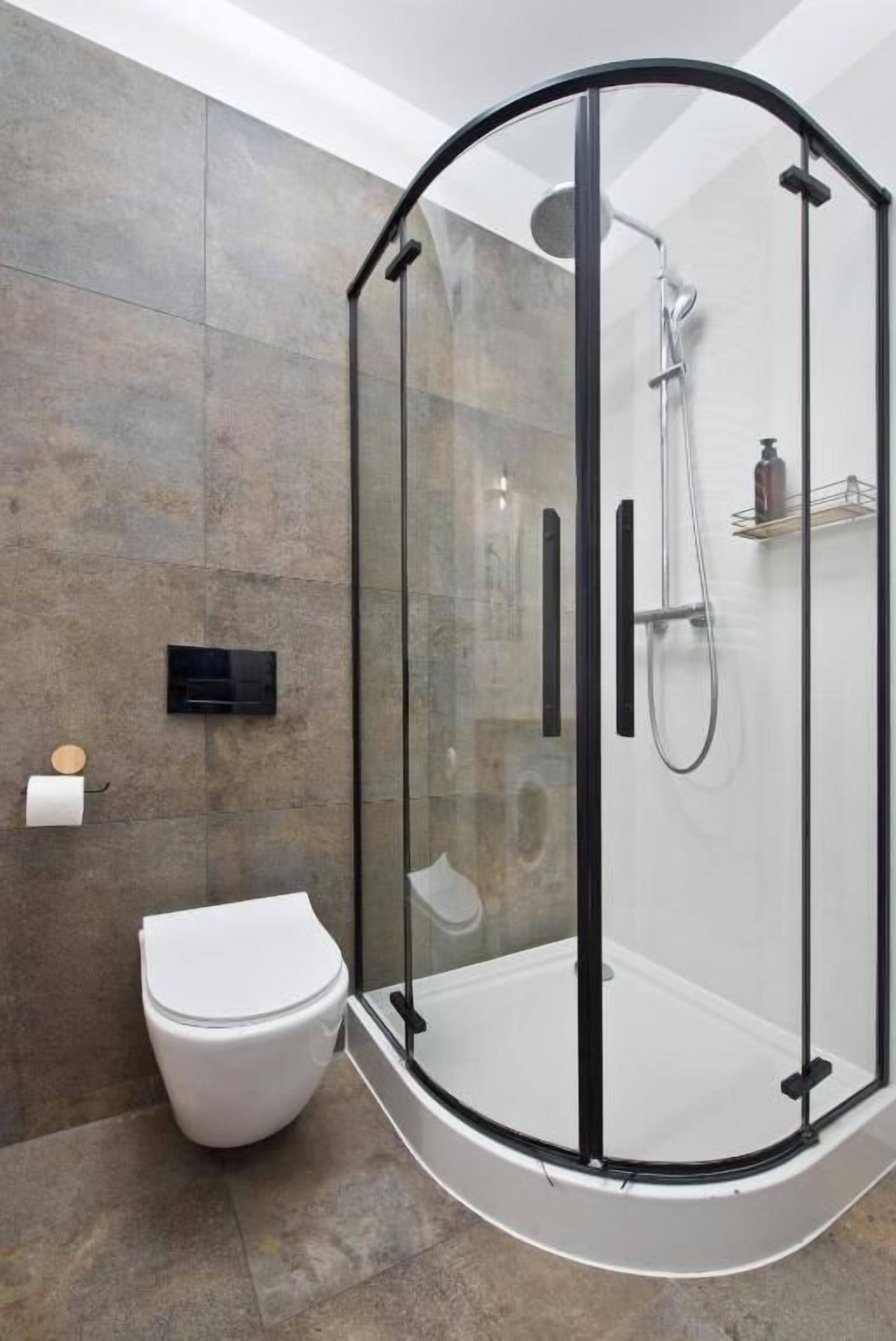 A modern bathroom with a glass-enclosed shower, a toilet, and a wall-mounted soap dispenser.