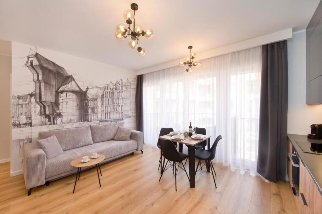 A modern living room with a grey sofa, a round coffee table, a dining table with chairs, and a large window with sheer curtains.