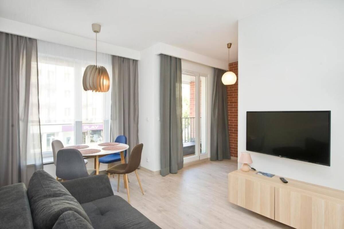 Ett modernt vardagsrum med en soffa, en tv som är monterad på väggen, en matplats med ett bord och stolar samt stora fönster med gardiner.