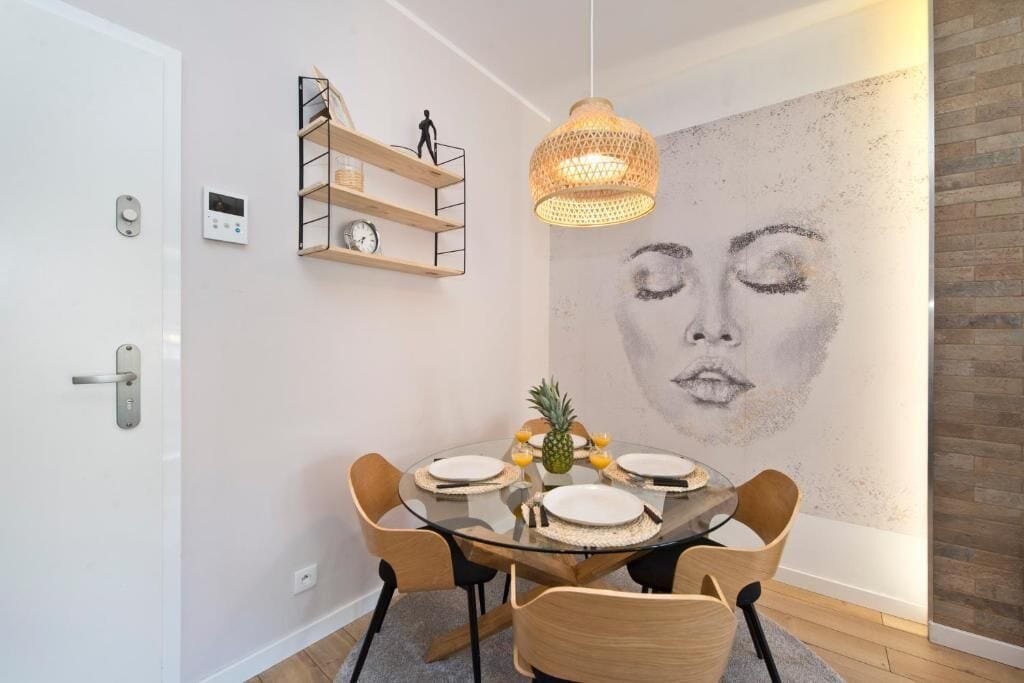 A dining area with a round glass table, wooden chairs, a pineapple centerpiece, and a wall-mounted shelf with a clock.
