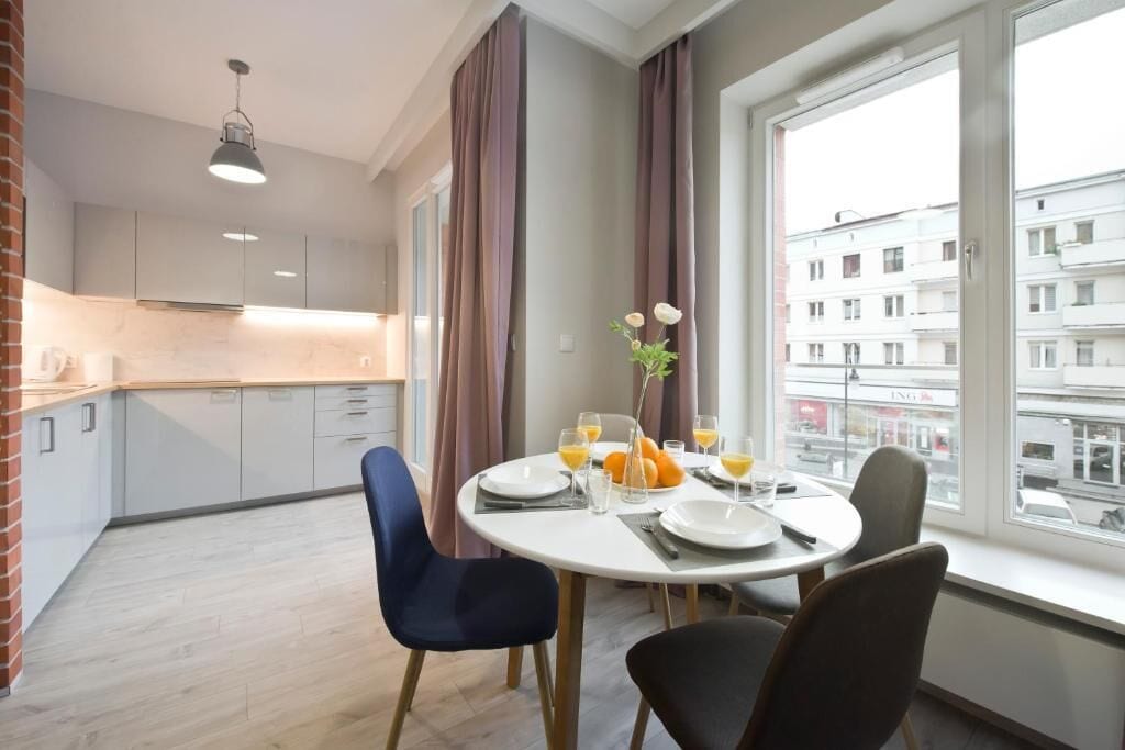 A dining area with a round table set for four, a vase with flowers, and a view of the city through large windows.