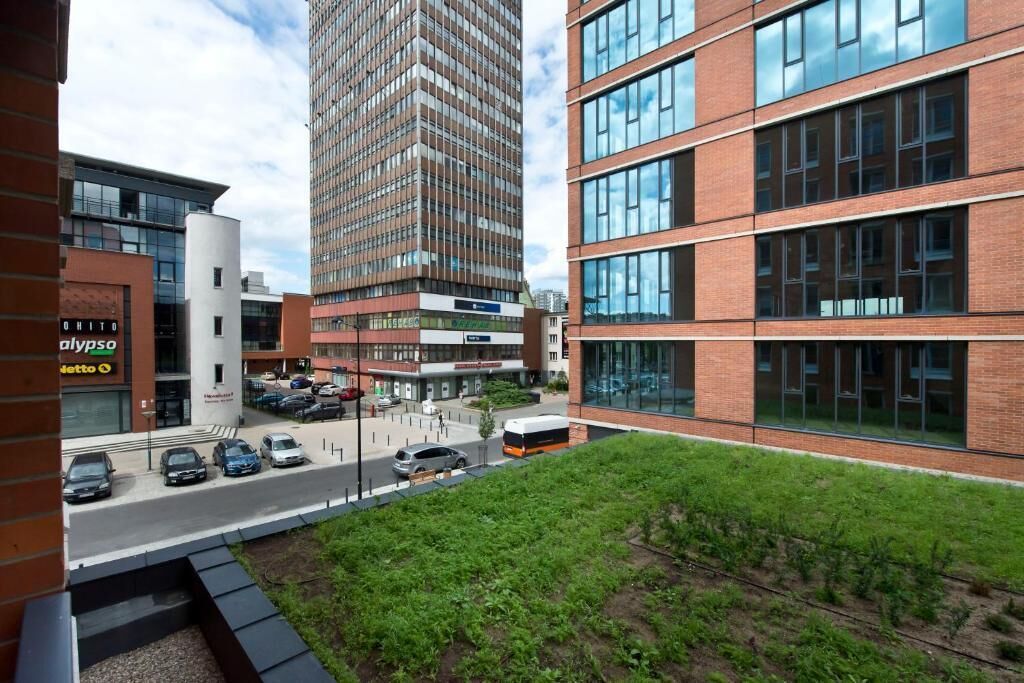 A modern building with multiple floors, large windows, and a parking area with cars.