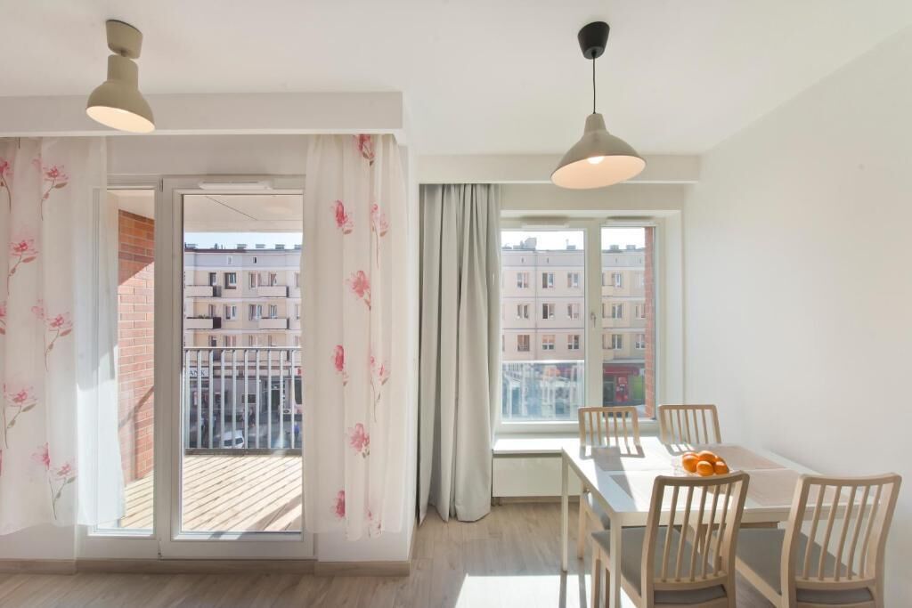 A dining area with a table and chairs, a window with a view of buildings, and a door leading to a balcony.