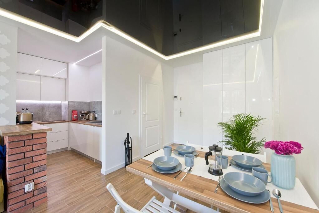 A modern kitchen with white cabinets, a brick accent wall, and a dining area with a wooden table set for four.