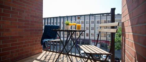 En balkon med trægulv, et metalbord med en potteplante og en blå stol.