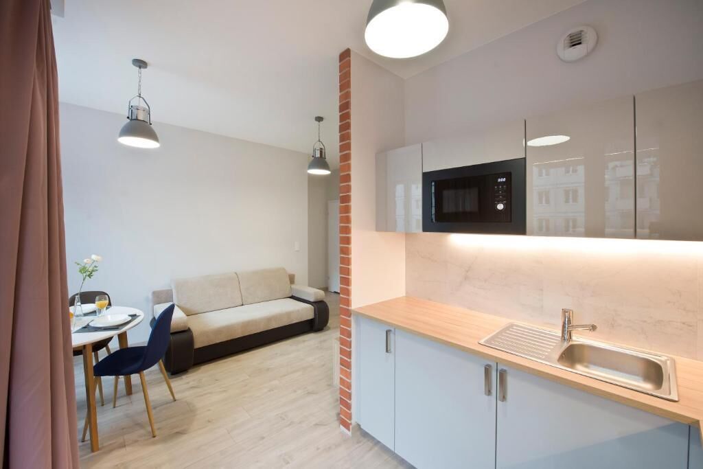 A modern kitchen with a microwave, sink, and wooden countertop. There is a dining area with a table and chairs, and a sofa.