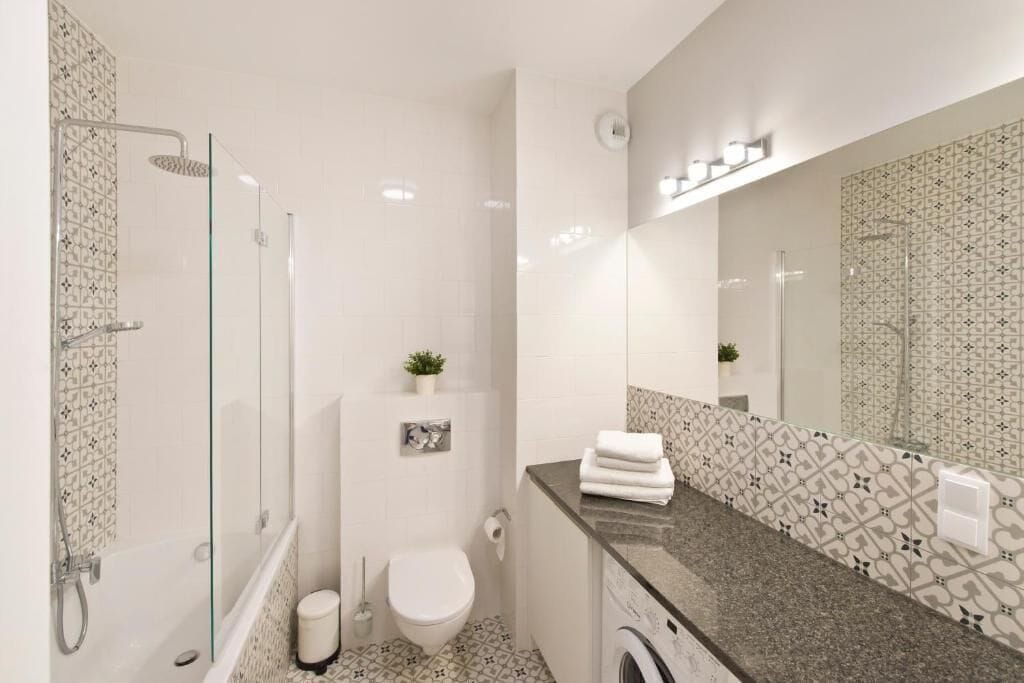 A modern bathroom with a glass-enclosed shower, a toilet, a washing machine, and a large mirror.