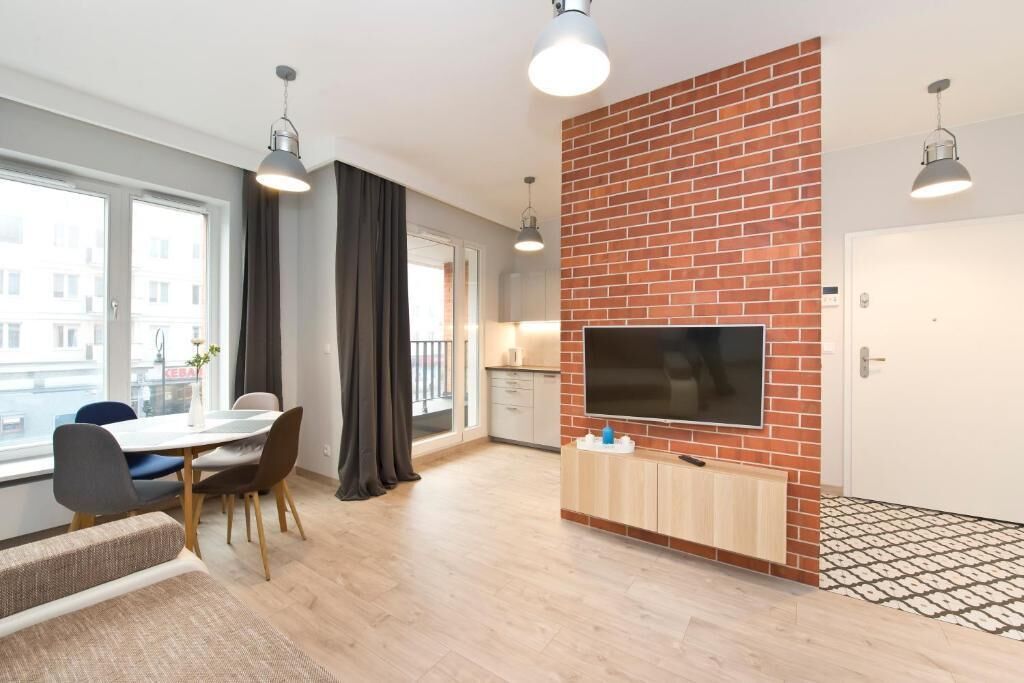 Een modern appartement met een eethoek, keuken, woonkamer met televisie en een groot raam met gordijnen.