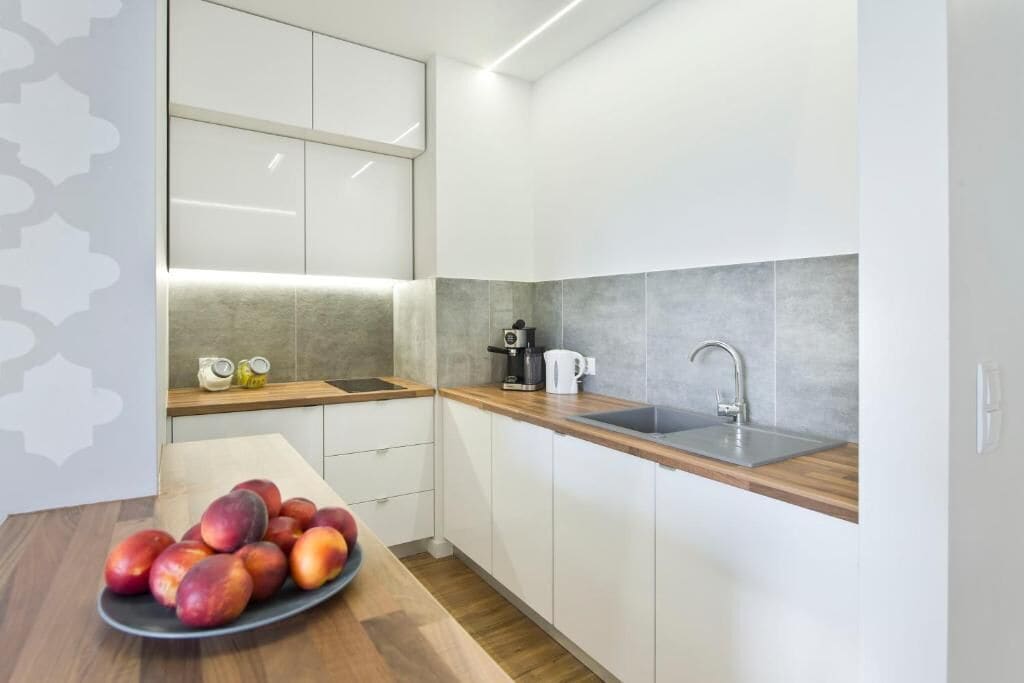 A modern kitchen with white cabinets, a wooden countertop, a sink, and a coffee maker.