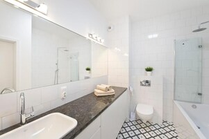 Un baño moderno con un espejo grande, un lavabo, un inodoro y una zona de ducha.