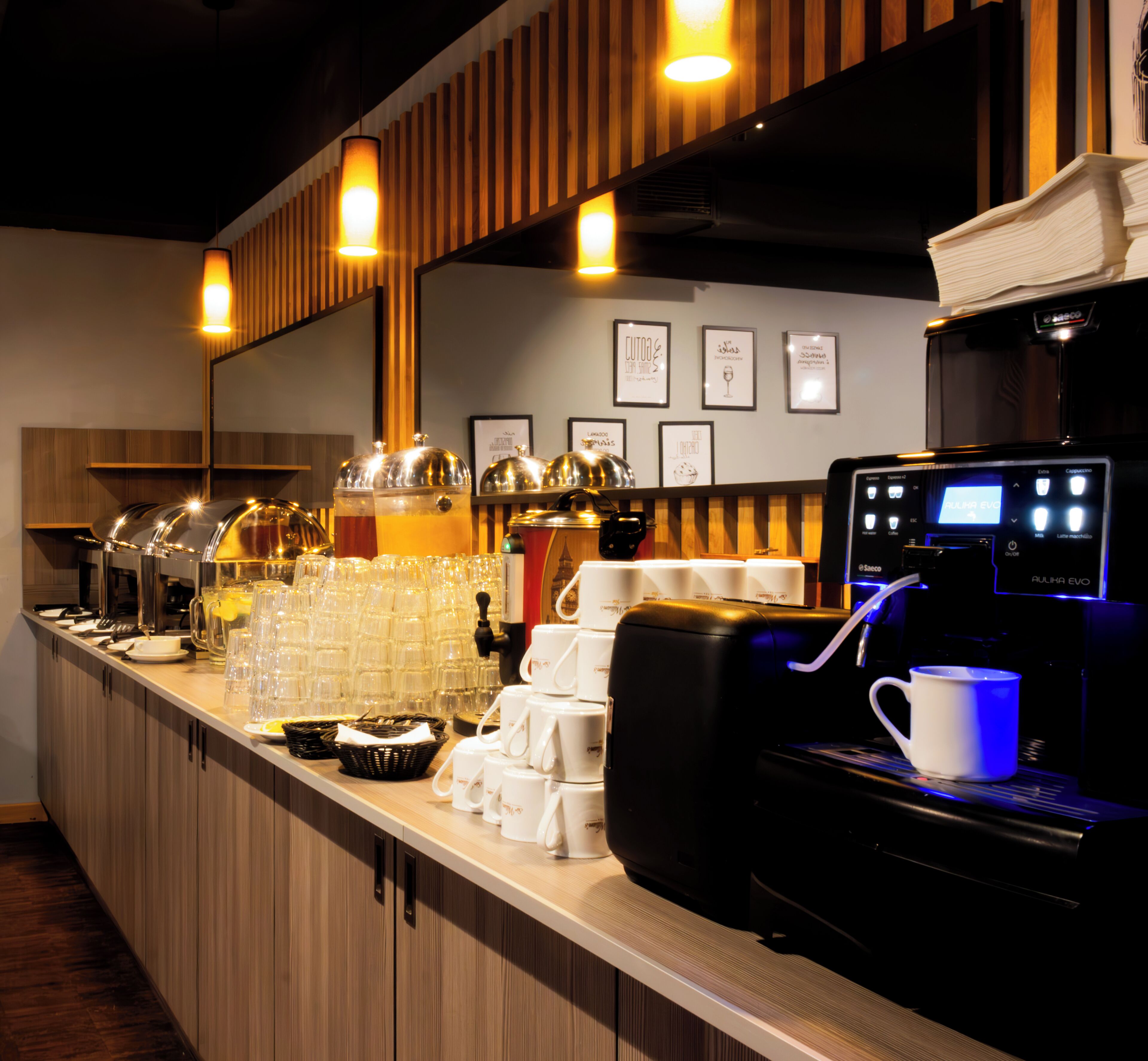 A coffee station with multiple coffee machines, a stack of white cups, and a beverage dispenser.