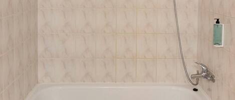 A bathroom with a white bathtub, a handheld showerhead, and a soap dispenser on the wall.