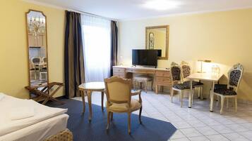 A hotel room with a bed, a desk, a television, and two dining tables with chairs.