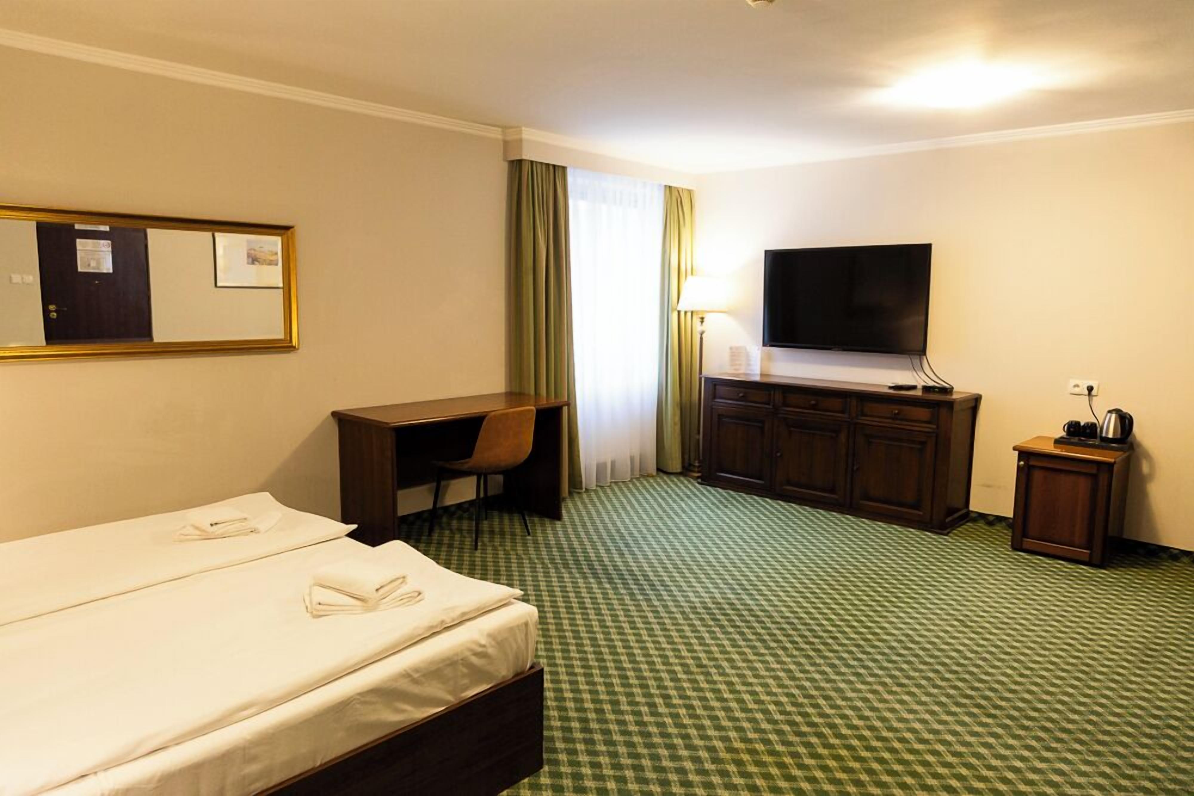 A hotel room with a bed, desk, chair, television, and a small cabinet.
