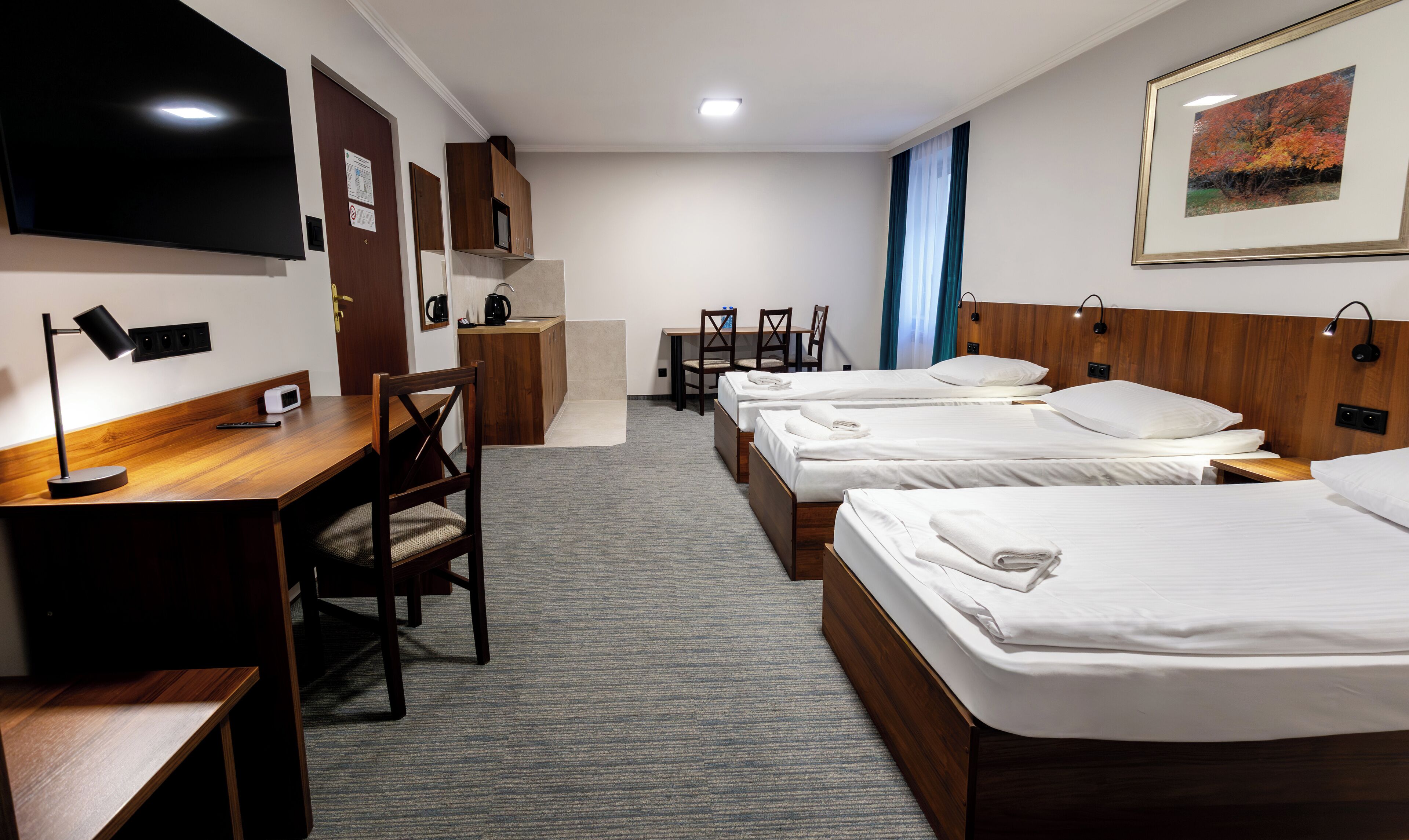 Ein Hotelzimmer mit drei Betten, einem Schreibtisch, einem Stuhl, einem Fernseher und einem gerahmten Bild an der Wand.