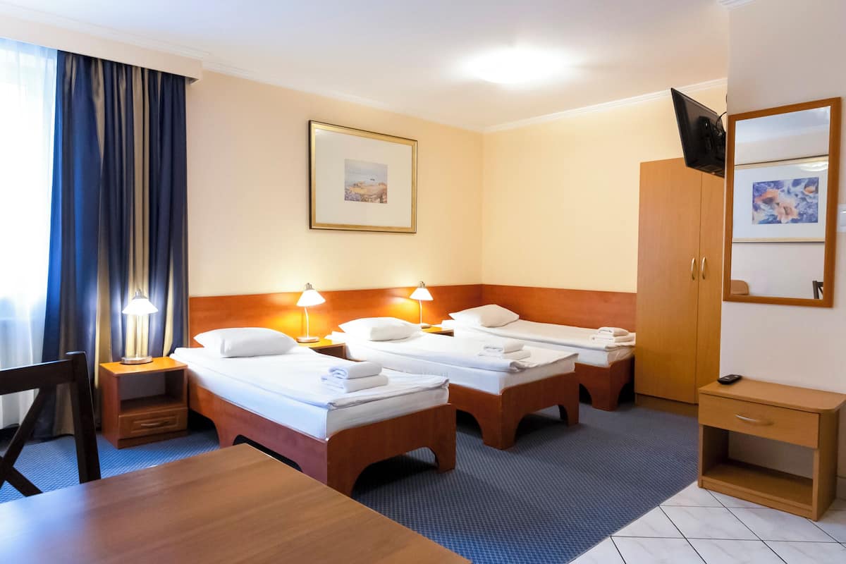 Een hotelkamer met drie eenpersoonsbedden, een houten bureau, een televisie en een kledingkast.