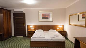 Una habitación de hotel con una cama doble, dos mesitas de noche con lámparas, un armario de madera, una puerta y un cuadro en la pared.