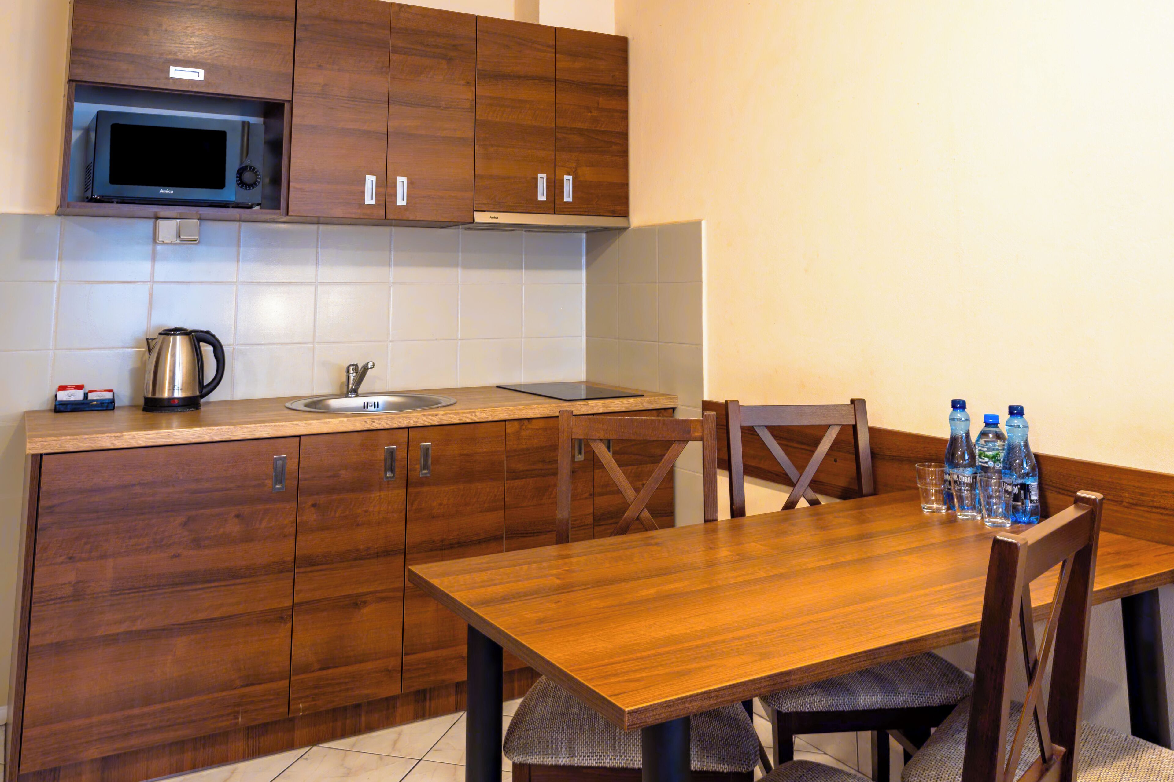 Een moderne keuken met houten kastjes, een magnetron, een waterkoker en een eettafel met stoelen.