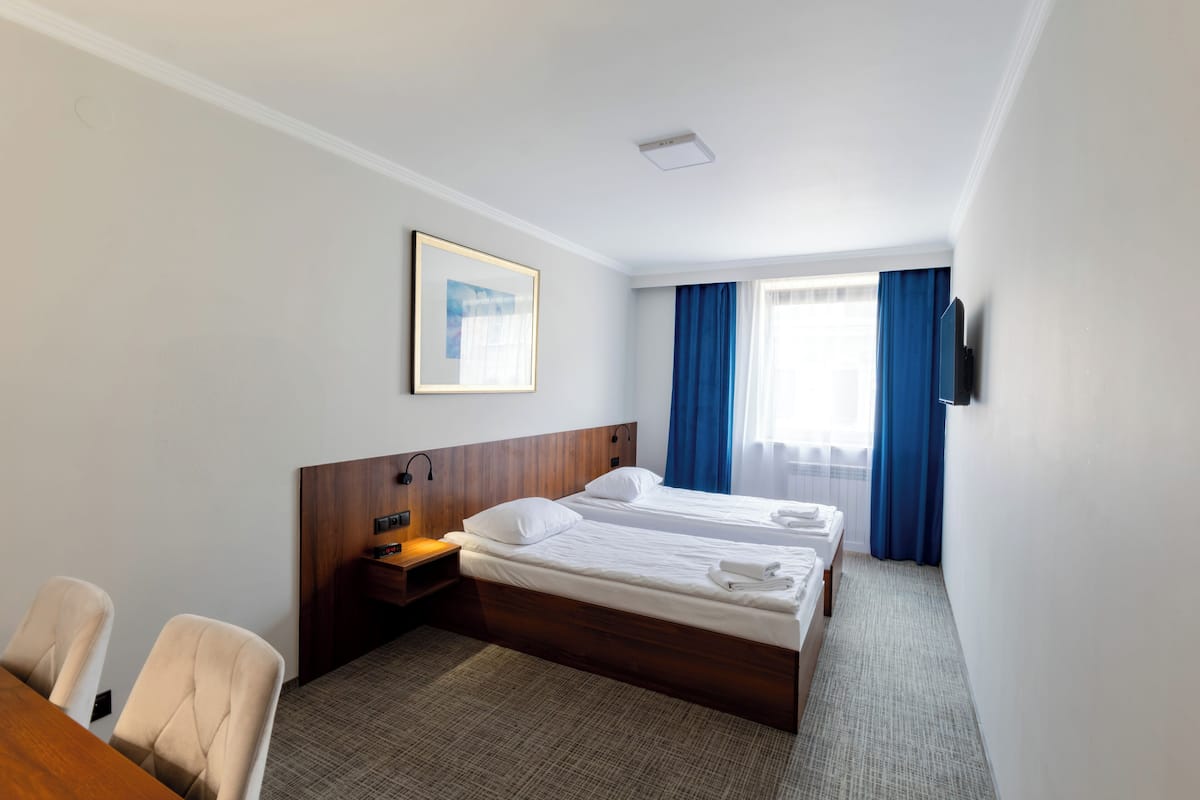 Een hotelkamer met twee bedden, een bureau, stoelen, een televisie en een raam met gordijnen.